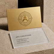 Gold metallic and frosted clear special material business cards with an Art Creators logo on a stone surface