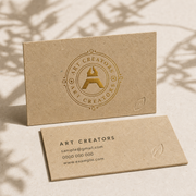Two brown kraft-style eco-friendly business cards with a gold Art Creators logo and sample contact details
